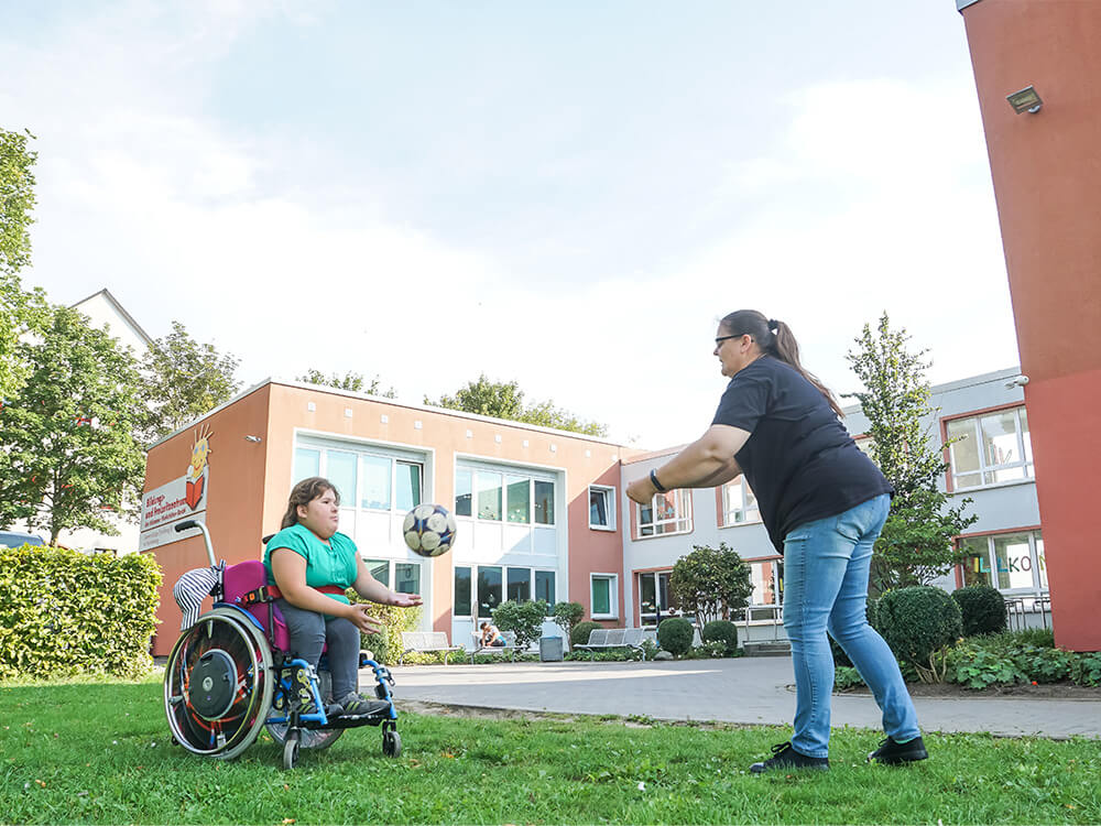 Kind im Rollstuhl und eine Frau beim Ballspiel
