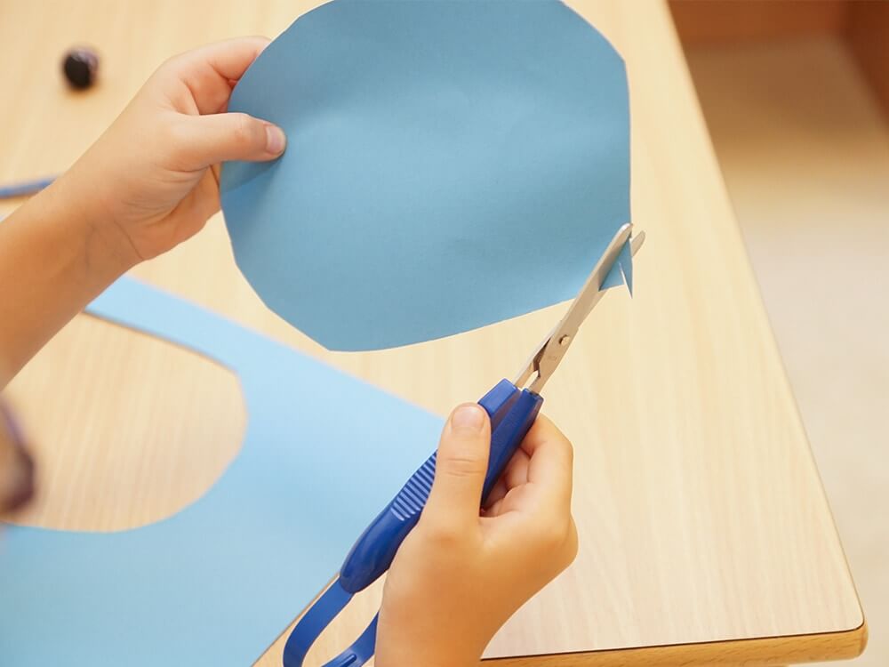 Kinderhände schneiden blaues Papier mit Schere aus