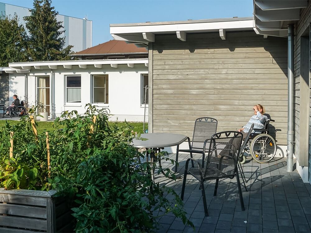 Eine Person im Rollstuhl schaut von der Terrasse in den Garten